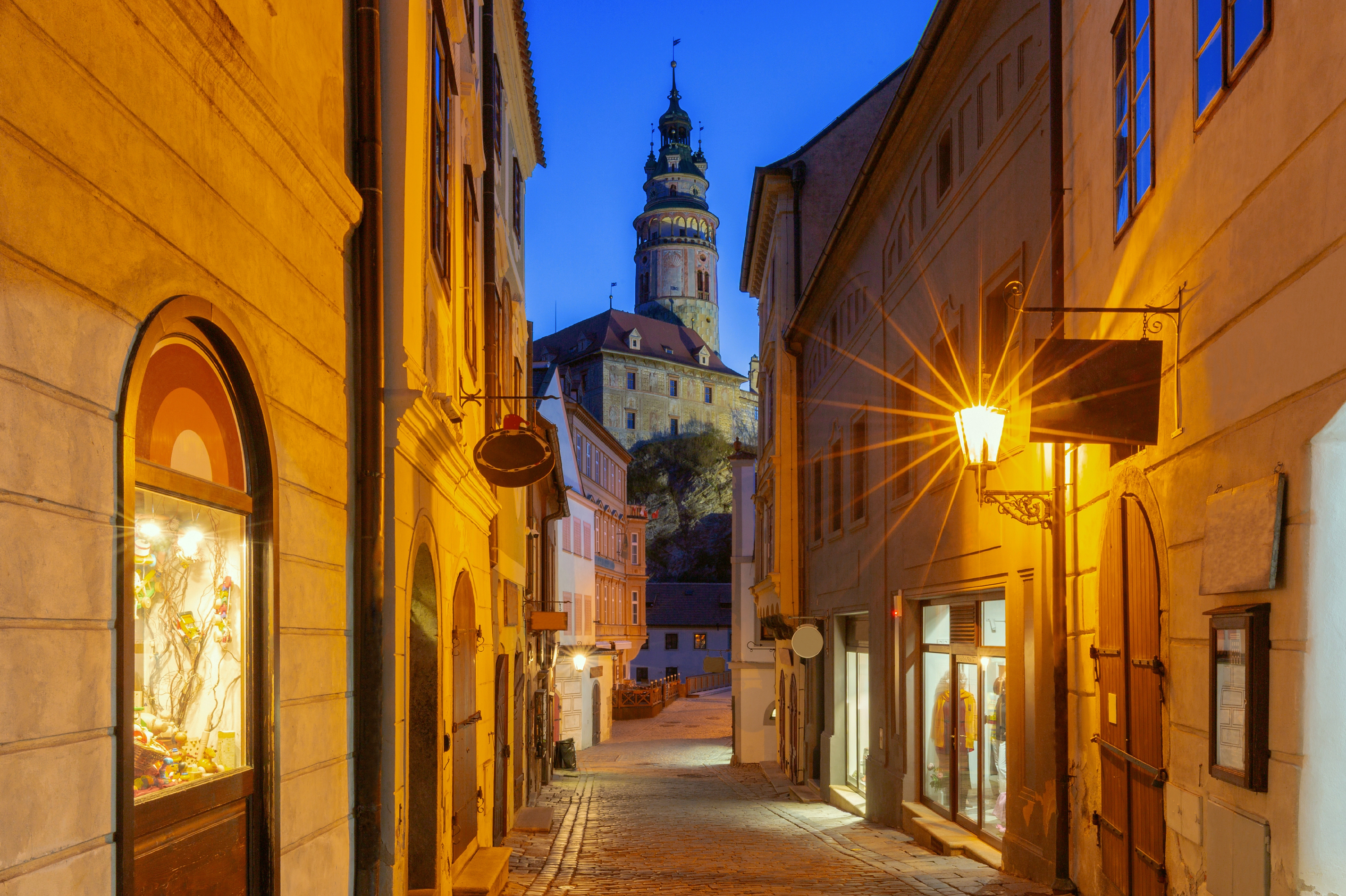 Cobblestone street in Český Krumlov old town with illuminated castle tower at blue hour