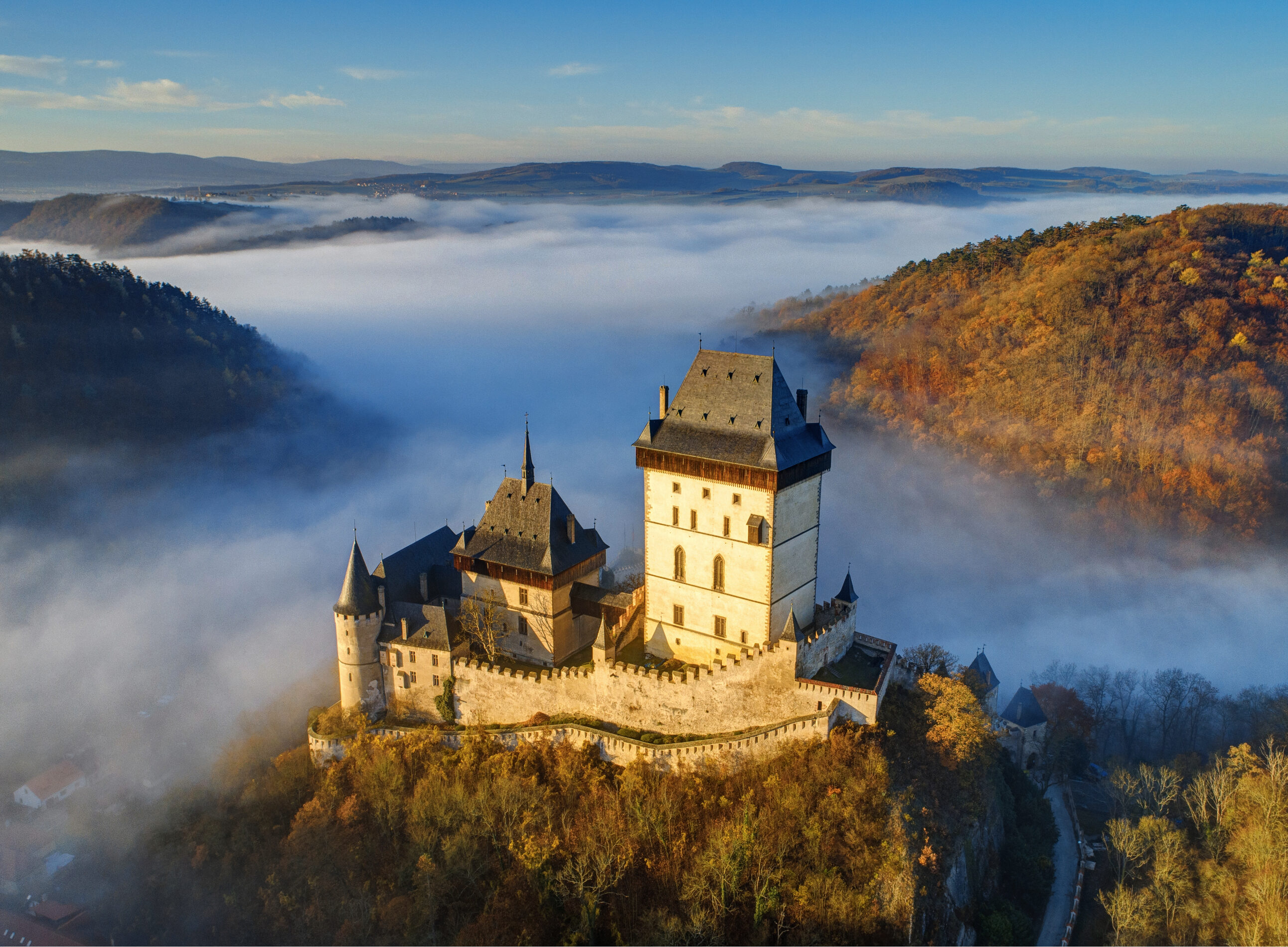 Hrad Karlštejn vystupující z&nbsp;ranní mlhy v&nbsp;údolí Berounky