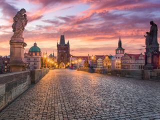 Karlův most při východu slunce s výhledem na Staroměstskou mosteckou věž a Vltavu v Praze