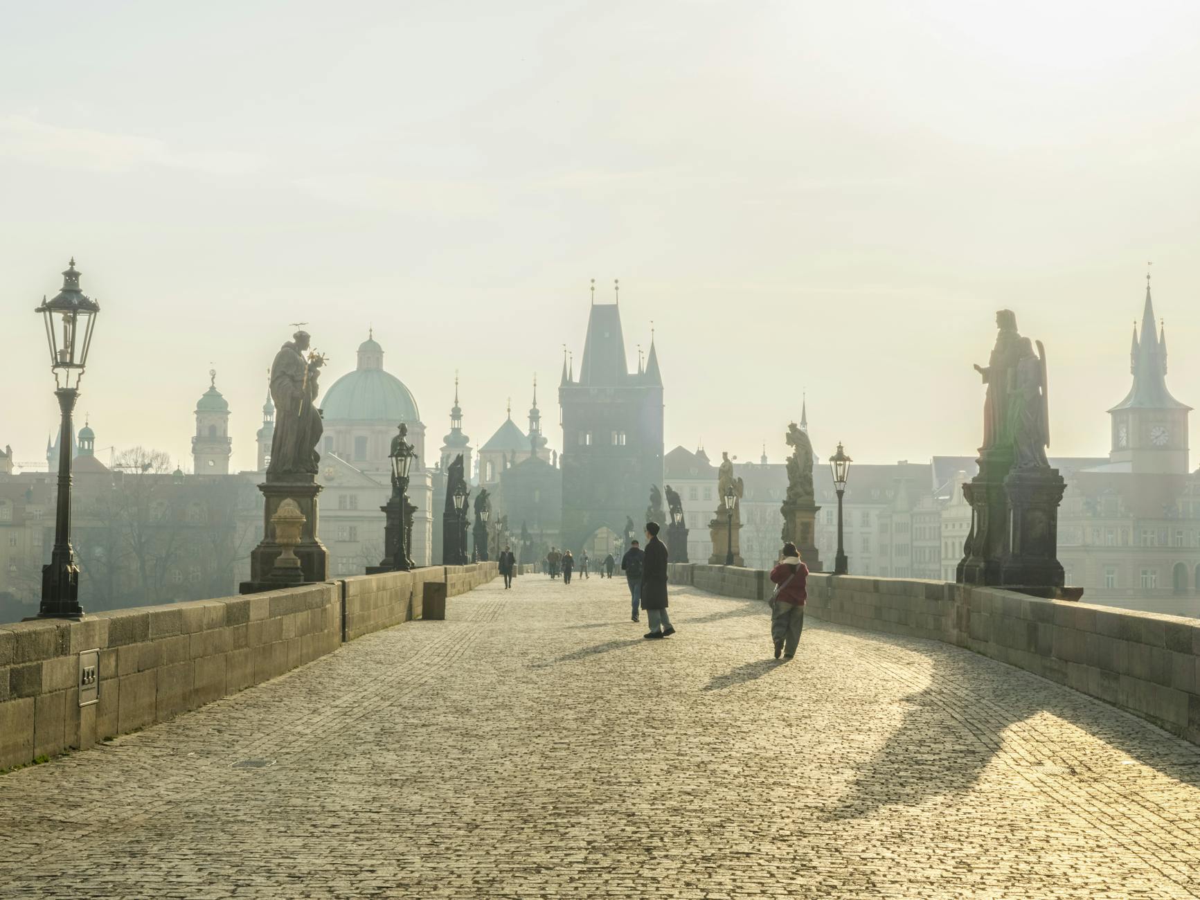 Karlův most v klidném ranním světle, turisté procházejí bezpečně historickým centrem Prahy