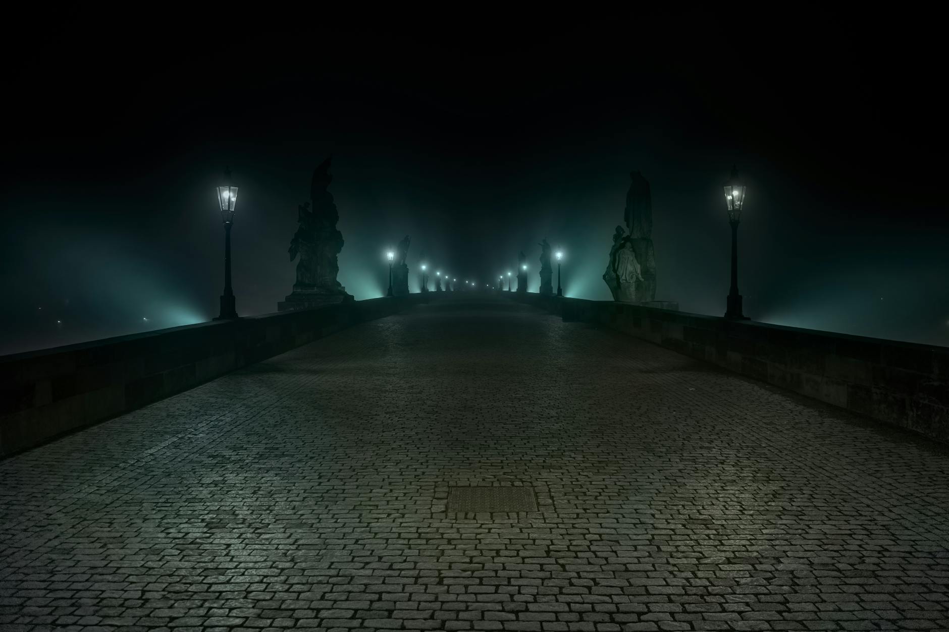 Tajemný noční pohled na Karlův most v Praze s mlhou a osvětlenými lucernami — atmosféra z literární procházky po místech Dana Browna