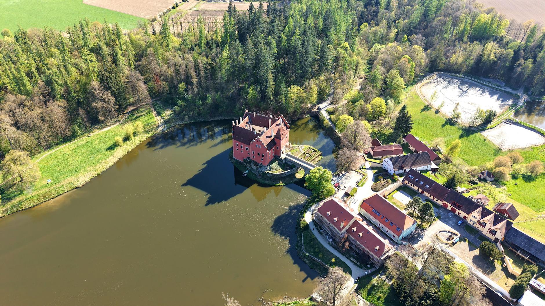 Stunning aerial photograph of a red-roofed water castle surrounded by lush greenery and a serene lake.