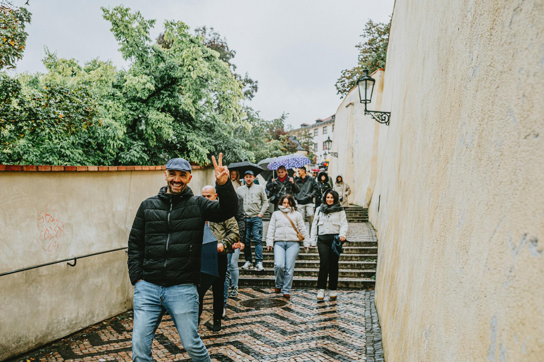Group of tourists walking down historic steps in Prague on a rainy day, capturing candid moments.
